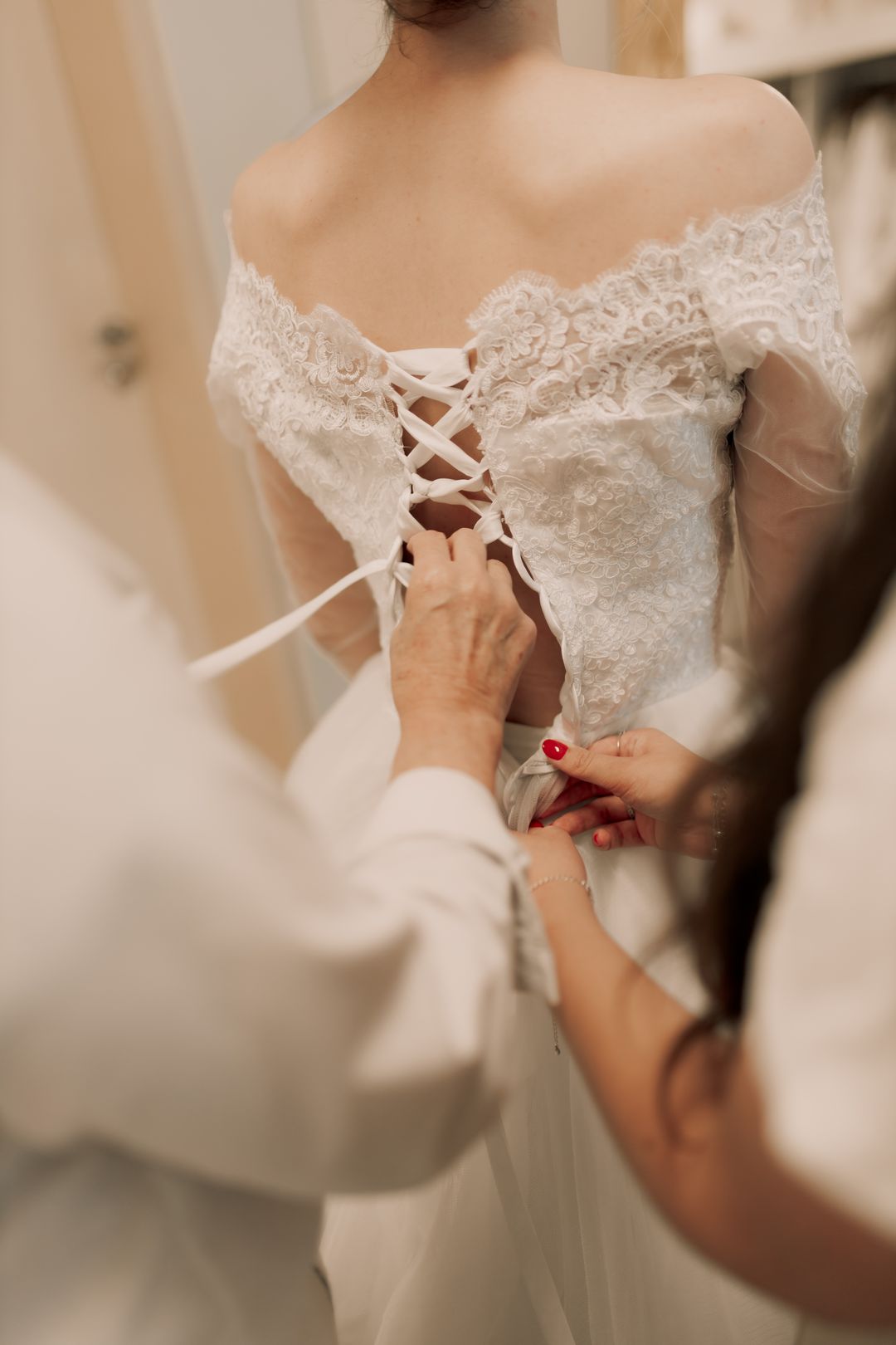 Fotografia de referência: mãos ajustando os laços de um vestido de noiva rendado, por Alexander Mass